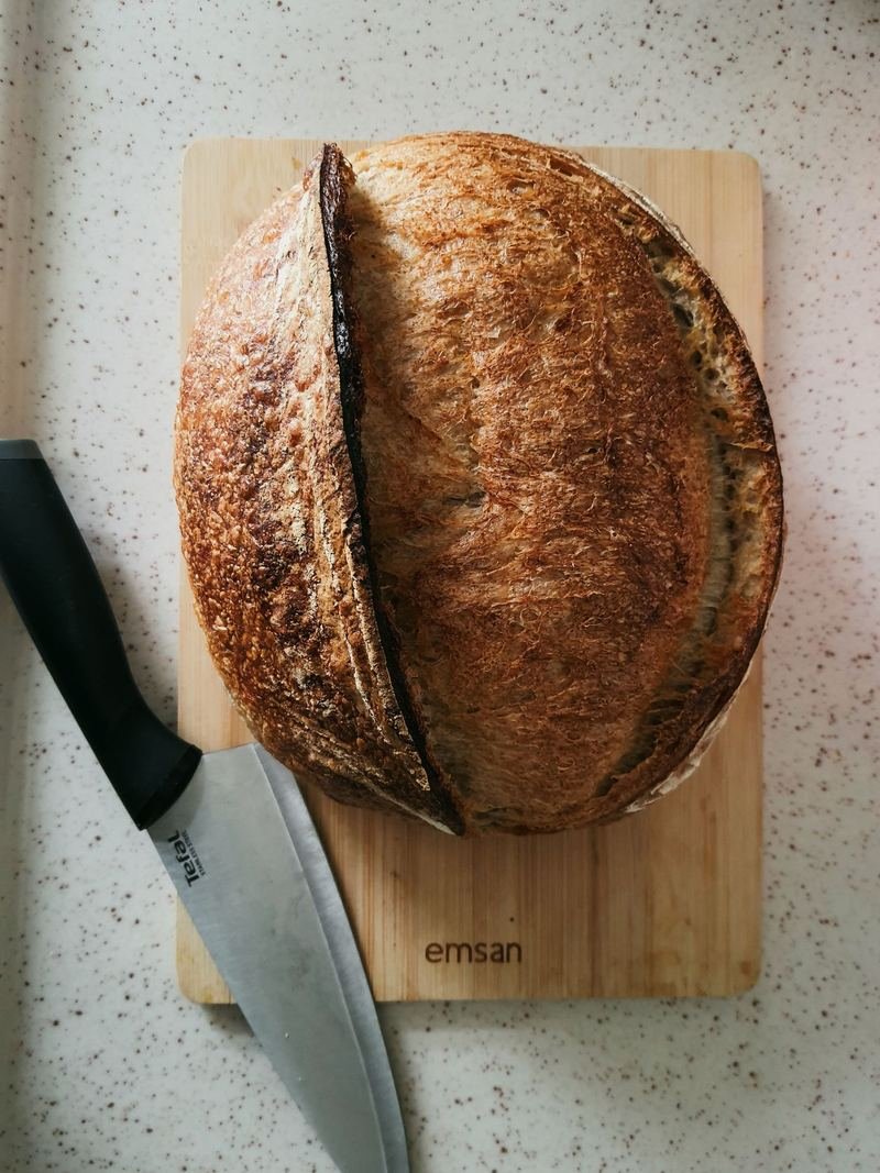 A round sourdough loaf on a wooden board beside a bread knife