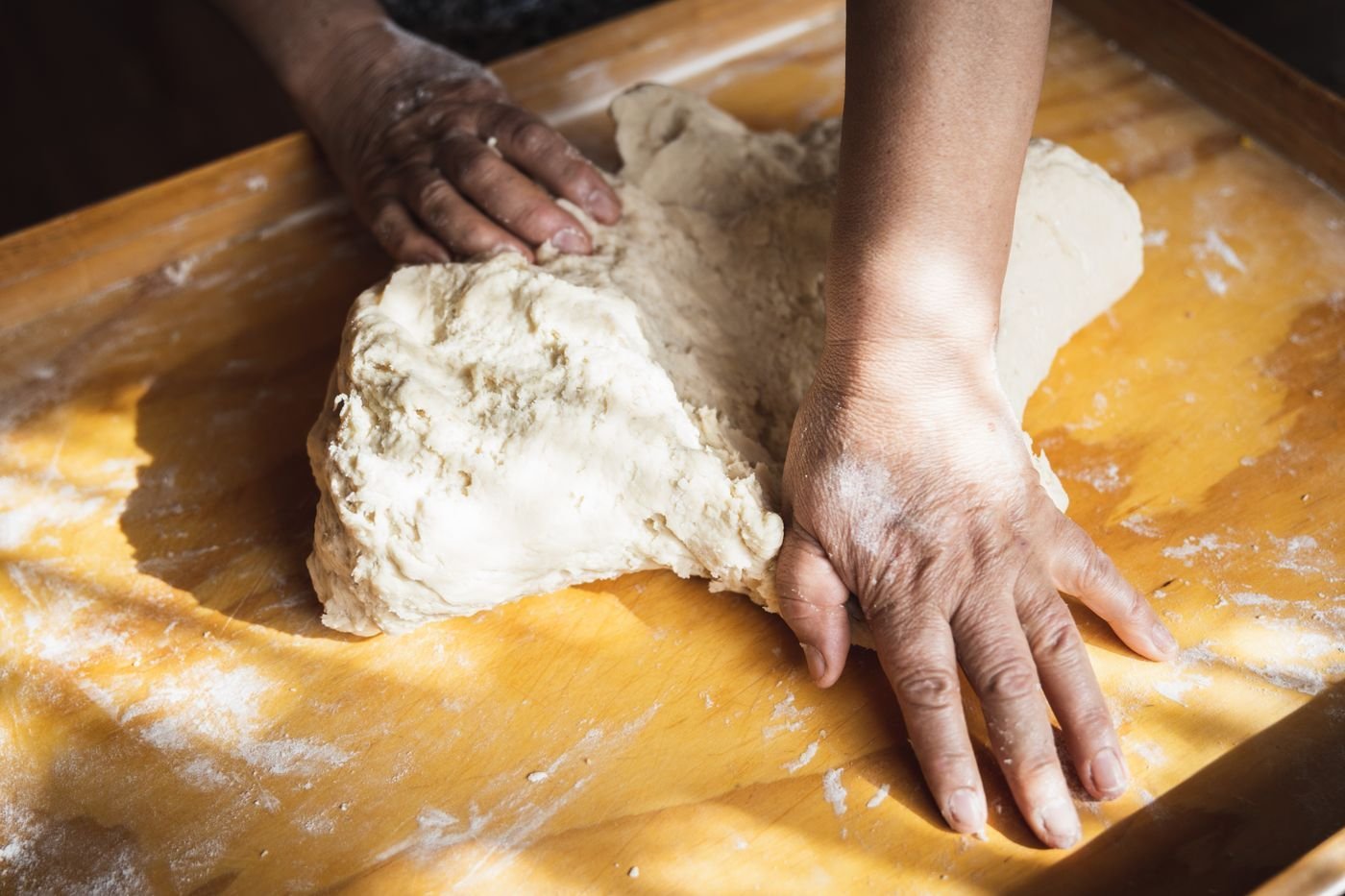 Hands kneading dough on a wooden bench